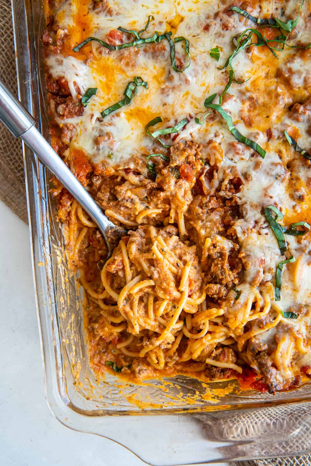 A top down shot of a spoon resting in a casserole dish full of spaghetti.