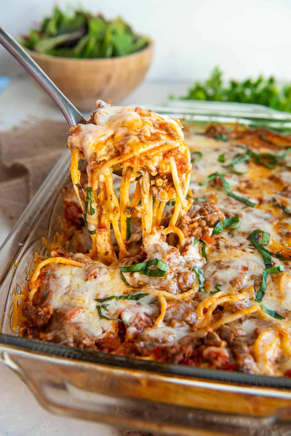 A spoon scooping spaghetti from a baking dish.