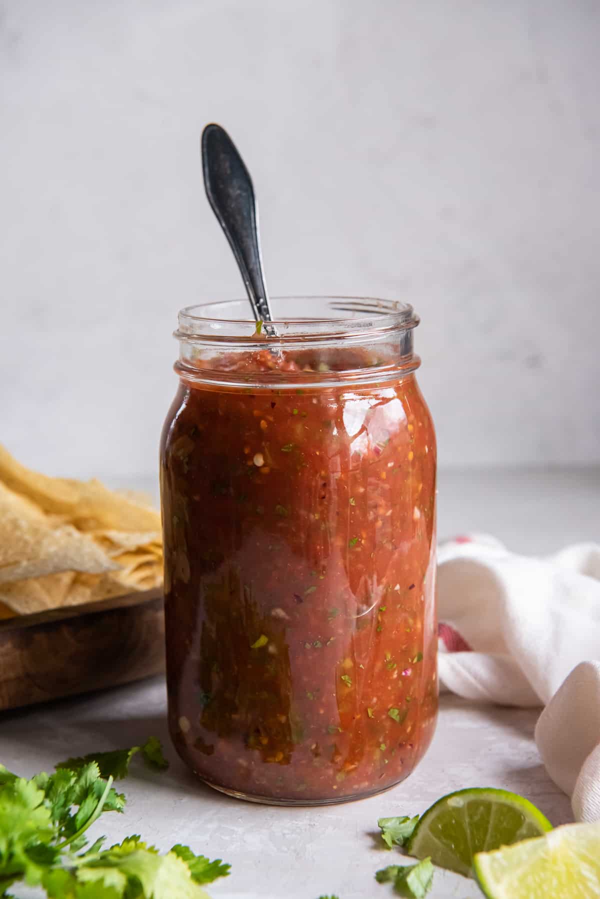 A spoon resting in a mason jar filled with salsa.