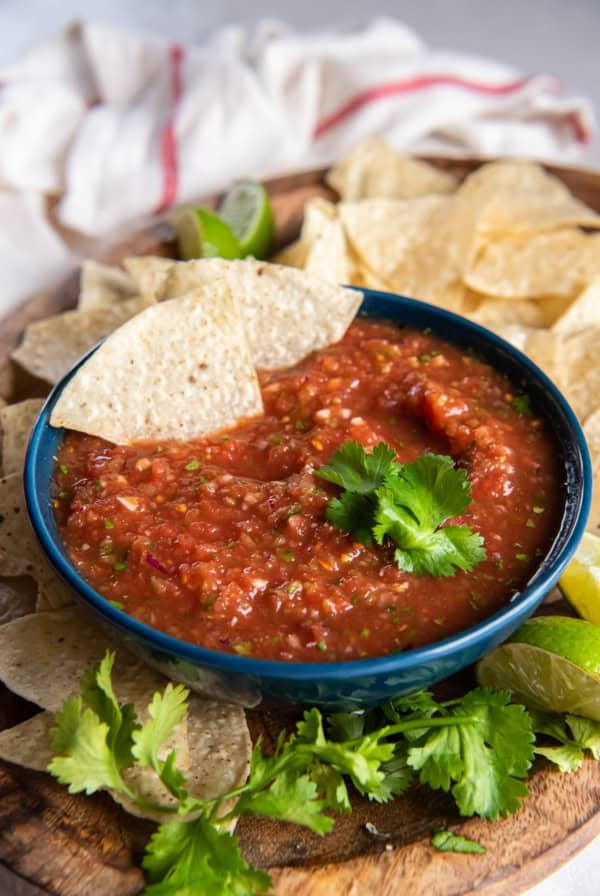 Two tortilla chips resting in a bowl of salsa on a platter with cilantro and more chips.