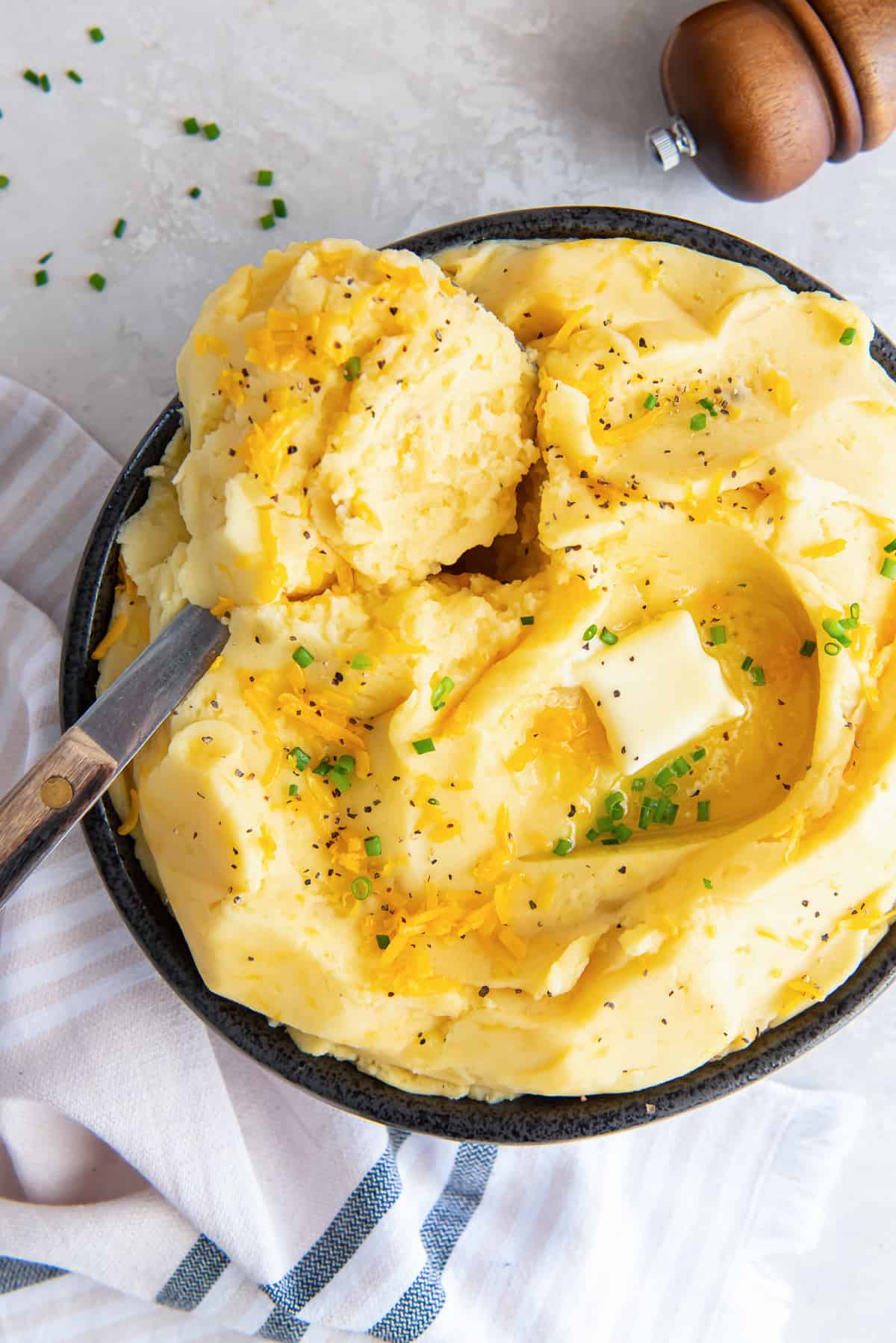 A serving spoon resting in a bowl of cheddar cheese mashed potatoes.