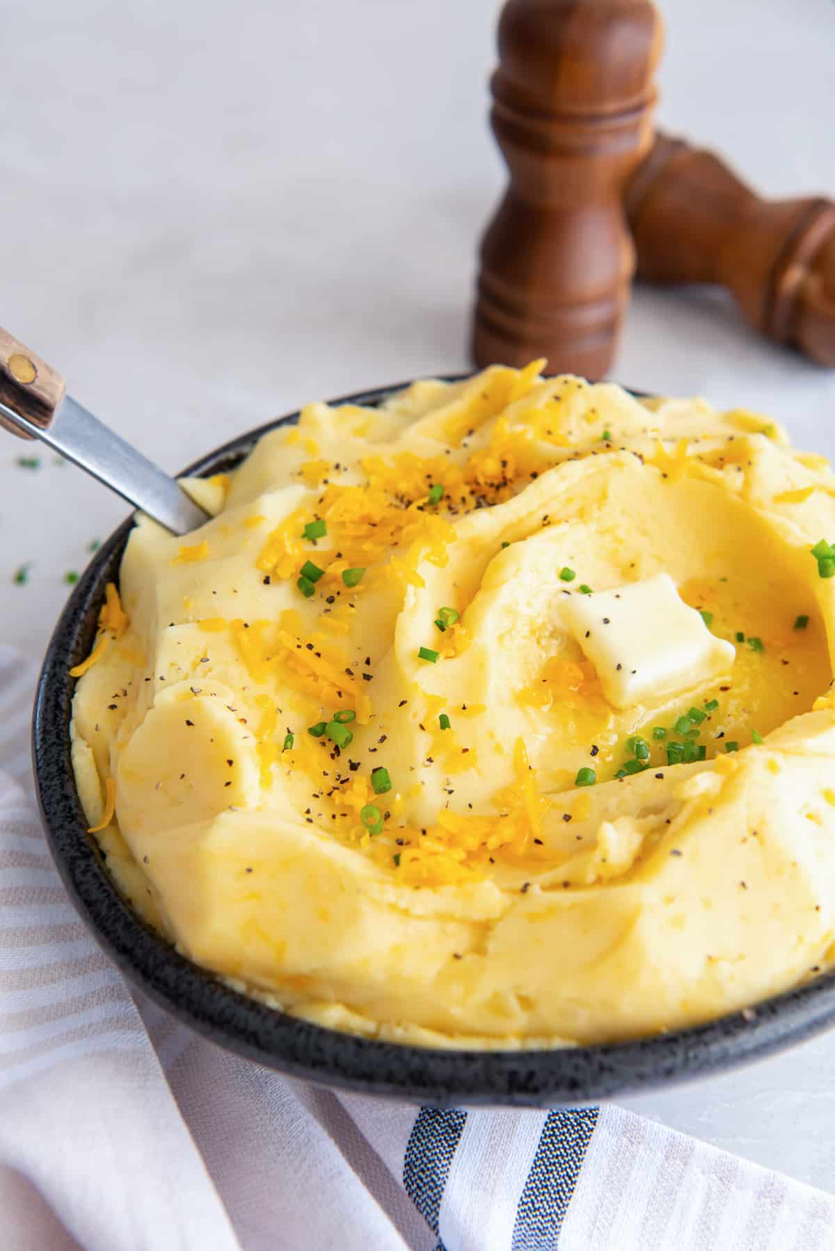Mashed potatoes with cheese in a dark bowl with a serving spoon.