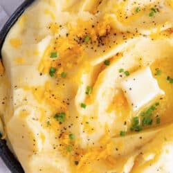 A top down shot of cheddar mashed potatoes topped with pepper and butter.