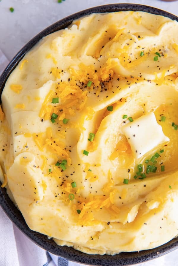 A top down shot of cheddar mashed potatoes topped with pepper and butter.