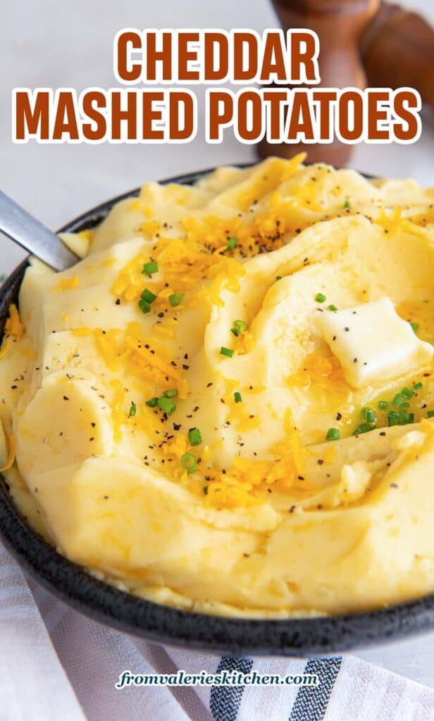 A close up of cheddar mashed potatoes in a dark bowl with text overlay.