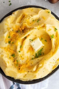 A top down shot of cheddar mashed potatoes topped with pepper, butter and chives.