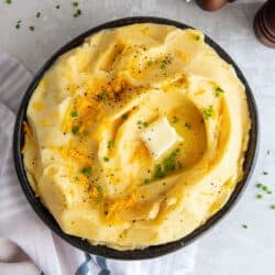 A top down shot of cheddar mashed potatoes topped with pepper, butter and chives.