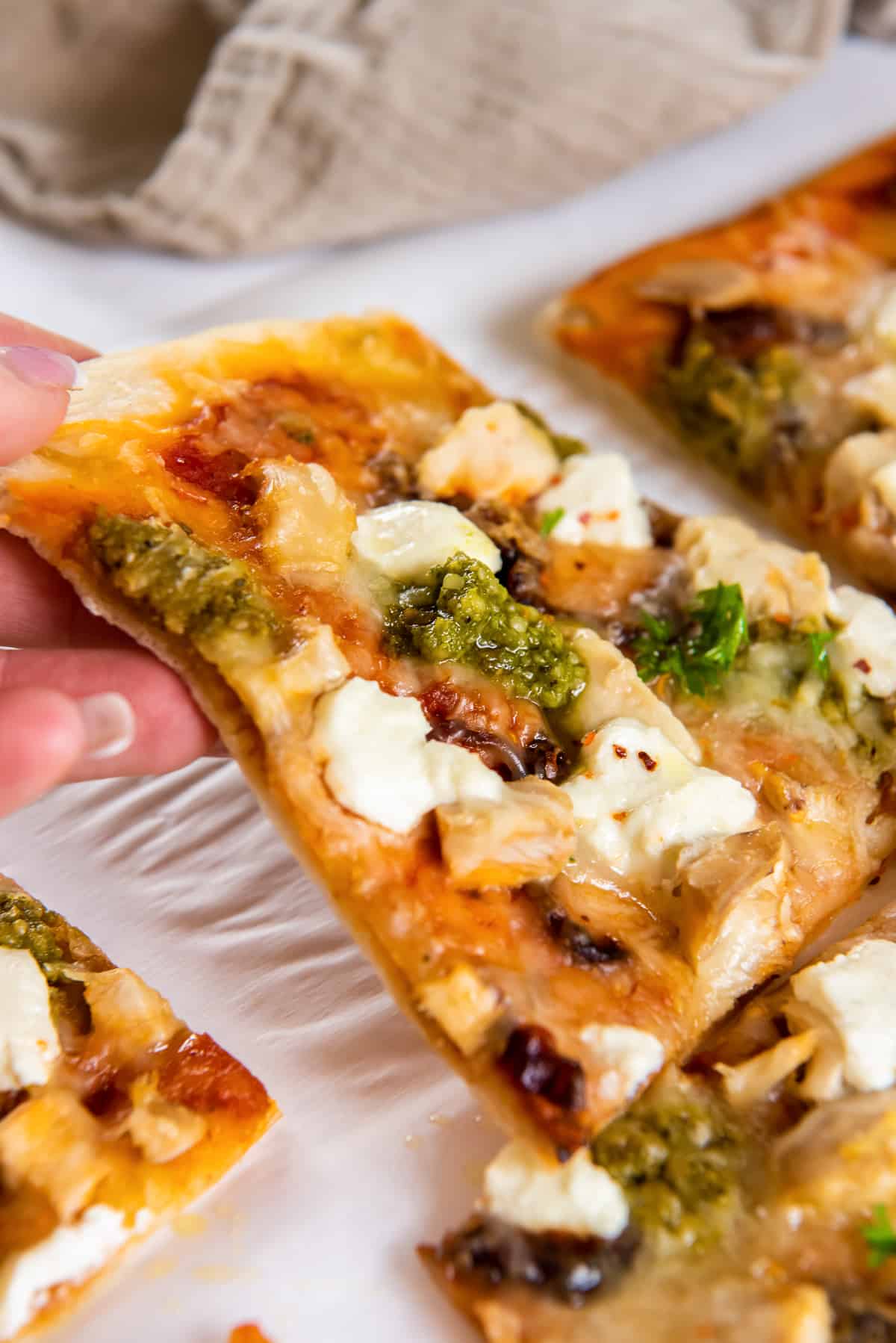 A hand lifting a slice of chicken pesto pizza.