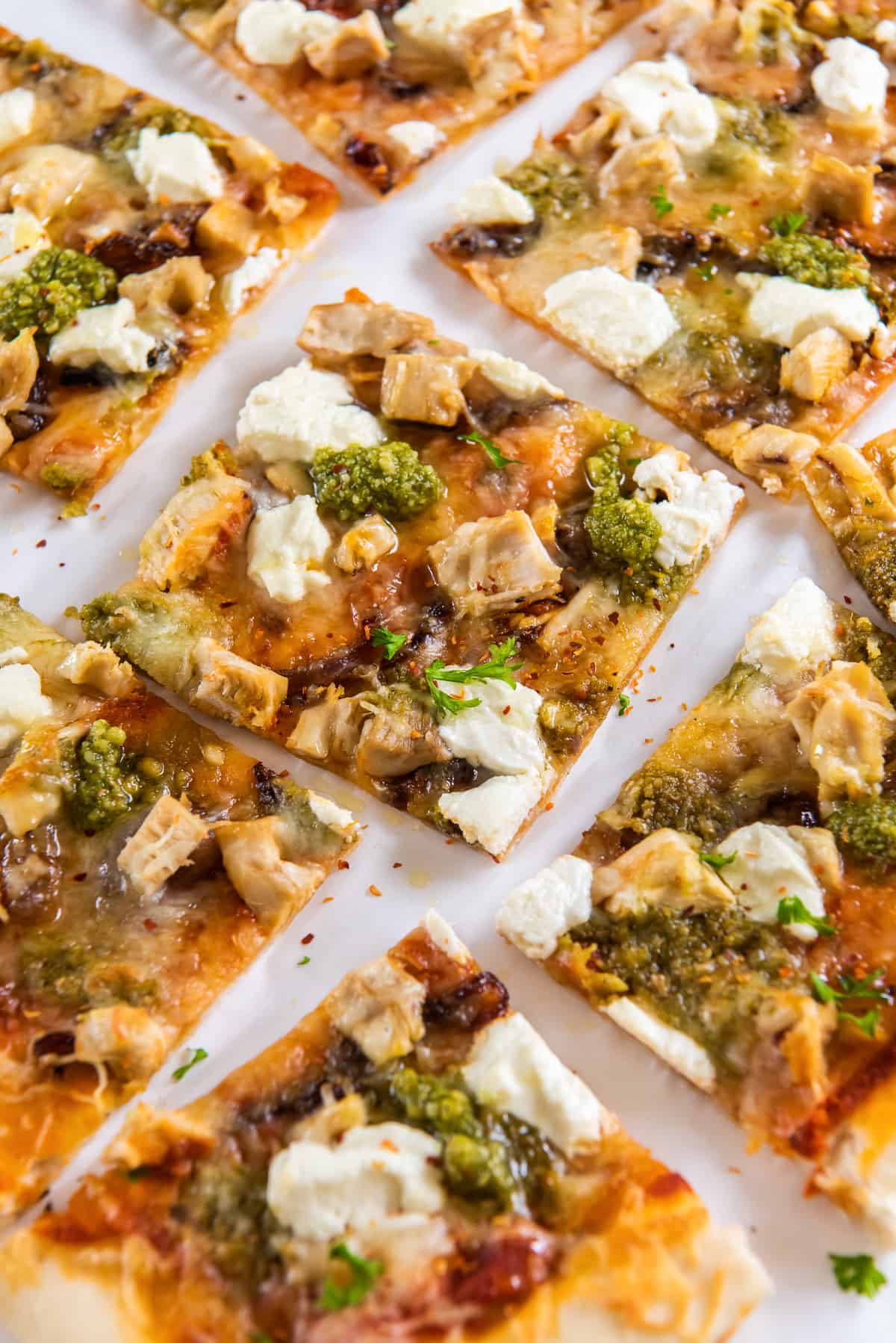 Square slices of chicken pesto pizza on parchment paper.