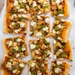 A top down shot of a sliced chicken pesto pizza next to a pizza cutter.