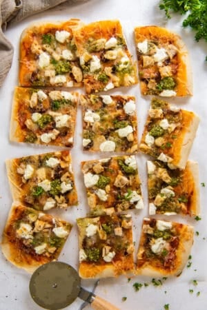 A top down shot of a sliced chicken pesto pizza next to a pizza cutter.