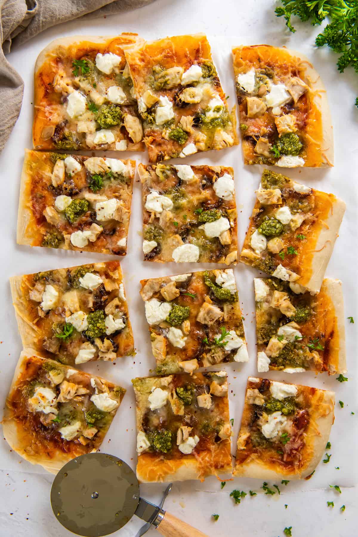 A top down shot of a sliced chicken pesto sheet pan pizza next to a pizza cutter.