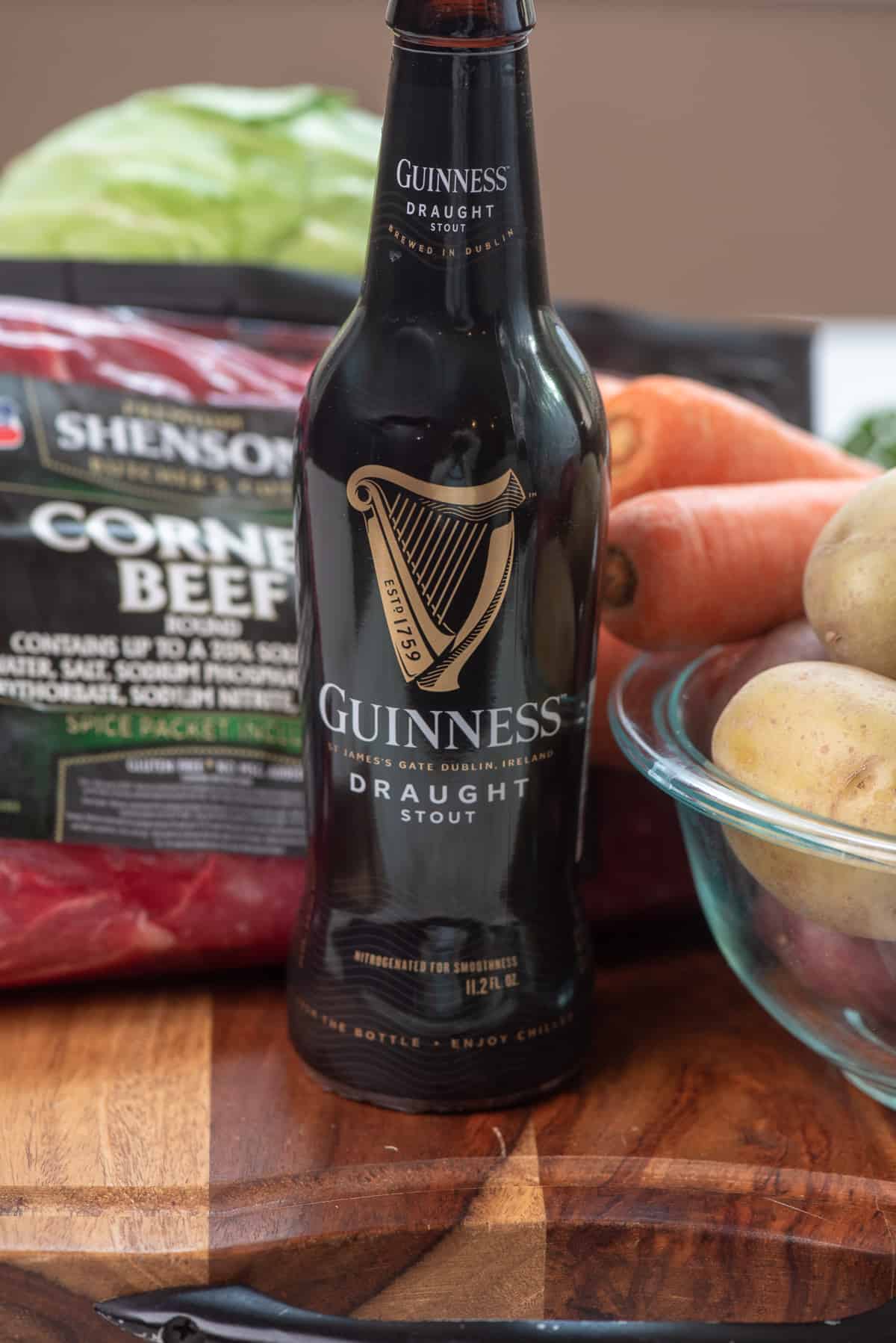 A bottle of Guinness beef on a wood board with a corned beef in the background.