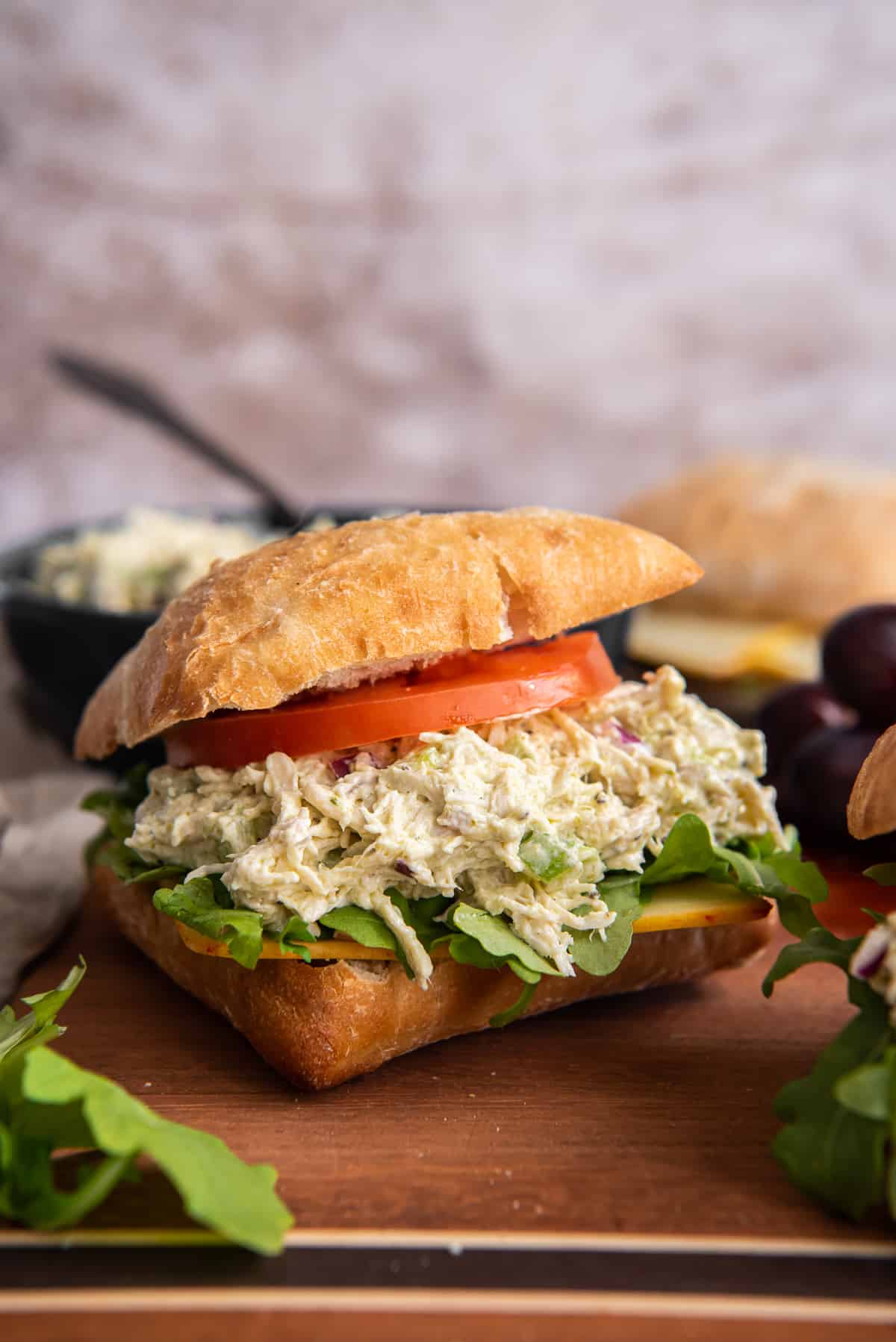 A pesto chicken salad sandwich with tomato and arugula on a wood board.