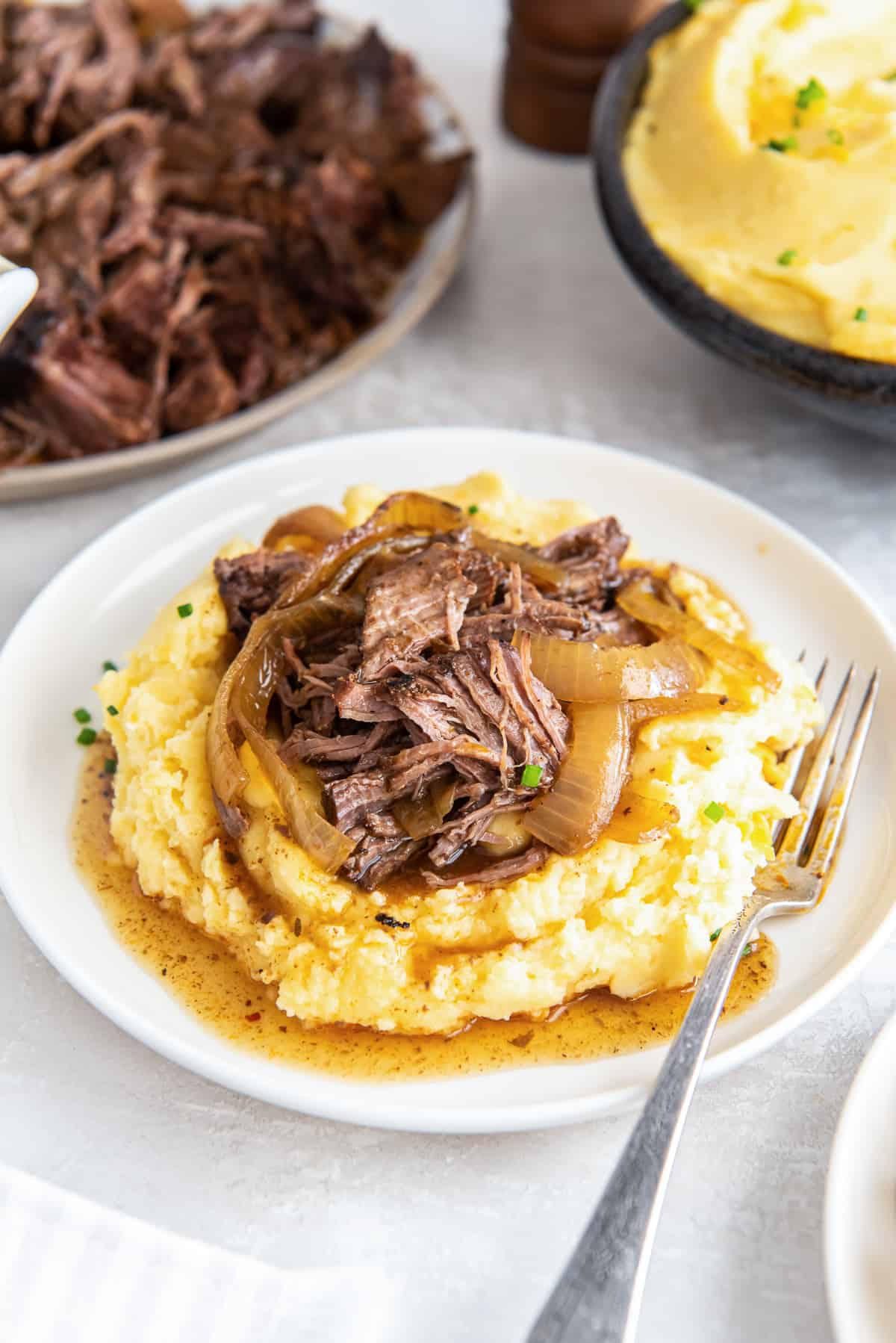 A plate with cheddar mashed potatoes topped with shredded beef and onions.