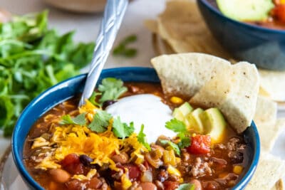 Taco soup in a blue bowl with a spoon topped with sour cream, cilantro, and avocado.