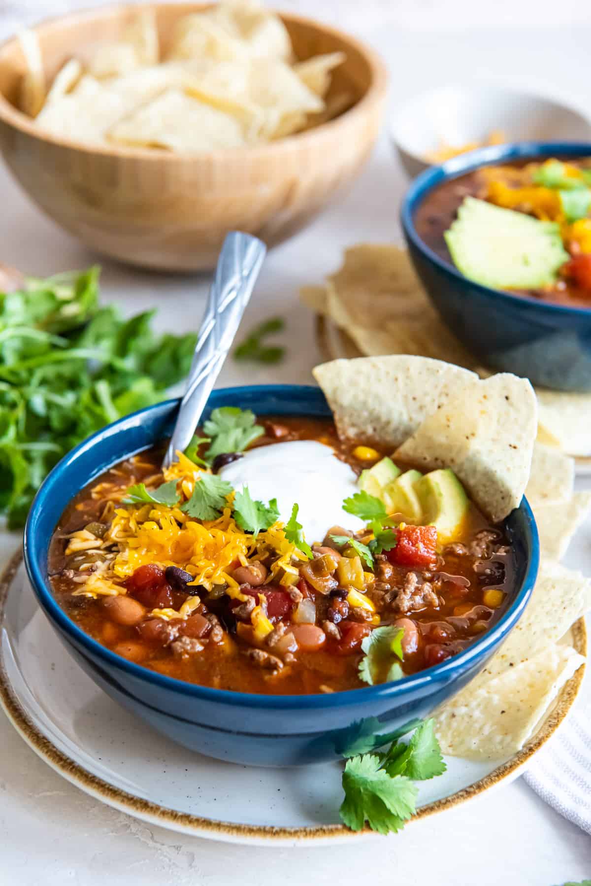 Taco soup in a blue bowl with a spoon topped with sour cream, cilantro, and avocado.