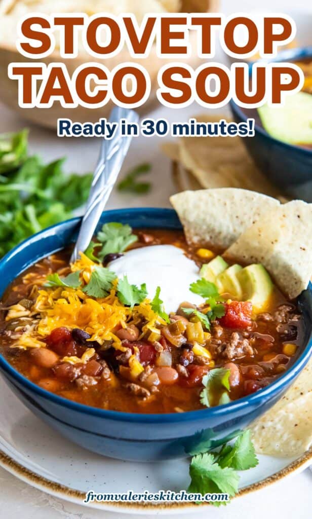 Taco soup in a blue bowl with a spoon topped with sour cream, cilantro, and avocado with text.