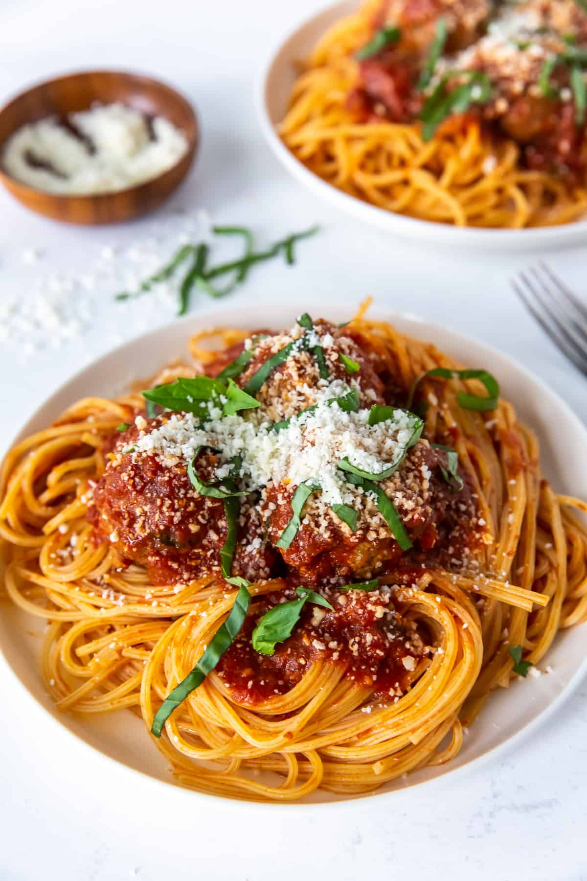 A dinner plate filled with homemade spaghetti and meatballs topped with basil and Parmesan.