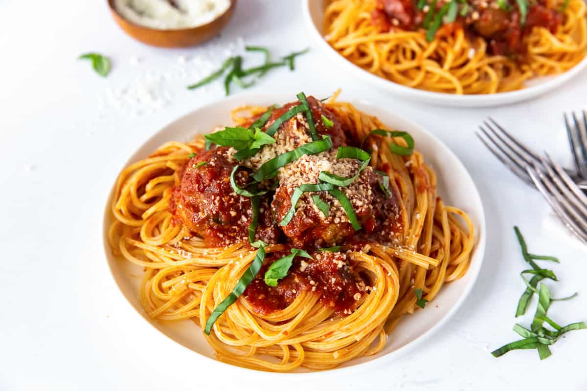 A dinner plate filled with homemade spaghetti and meatballs topped with basil and Parmesan.