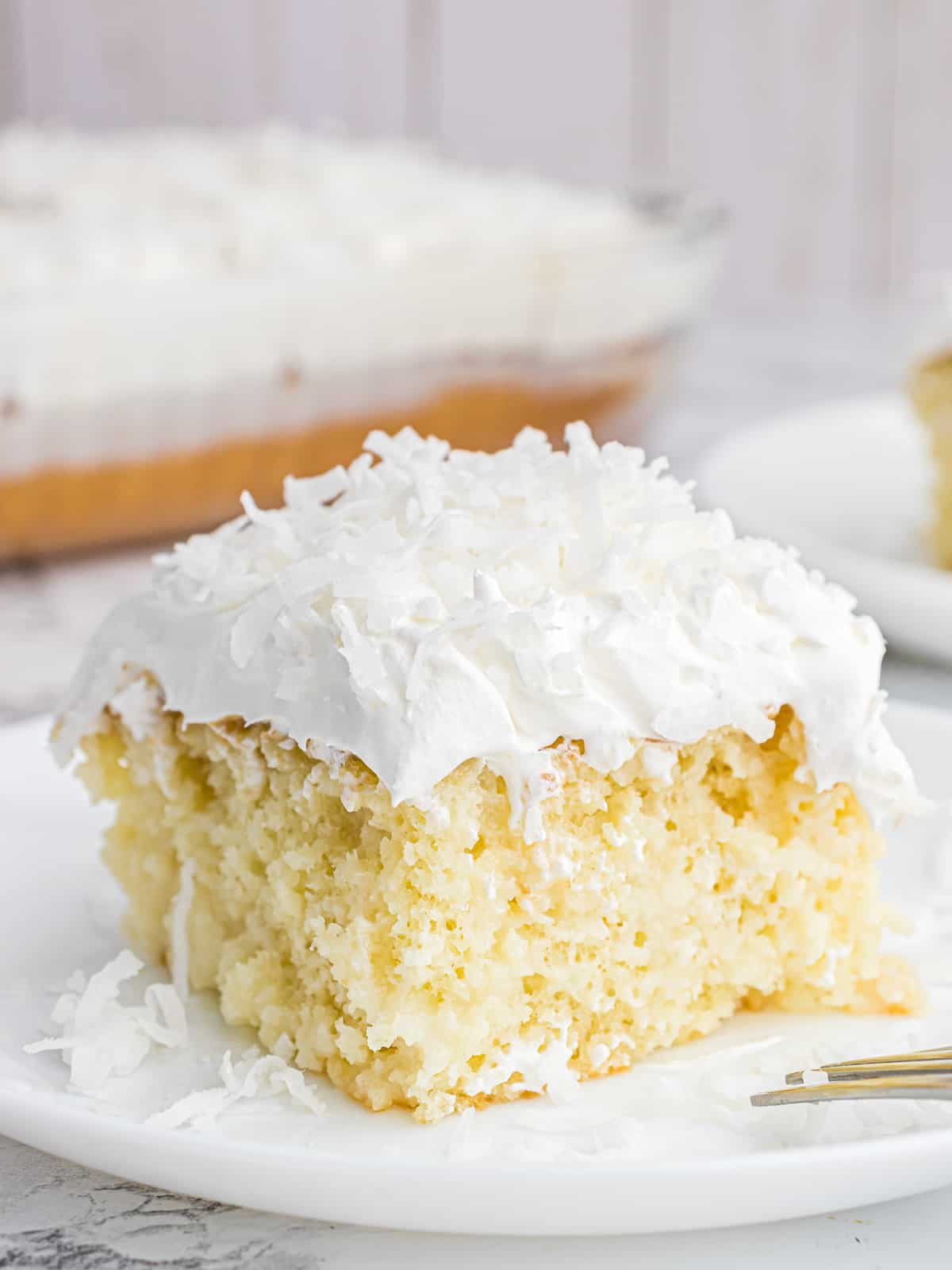 A slice of coconut poke cake on a white plate.