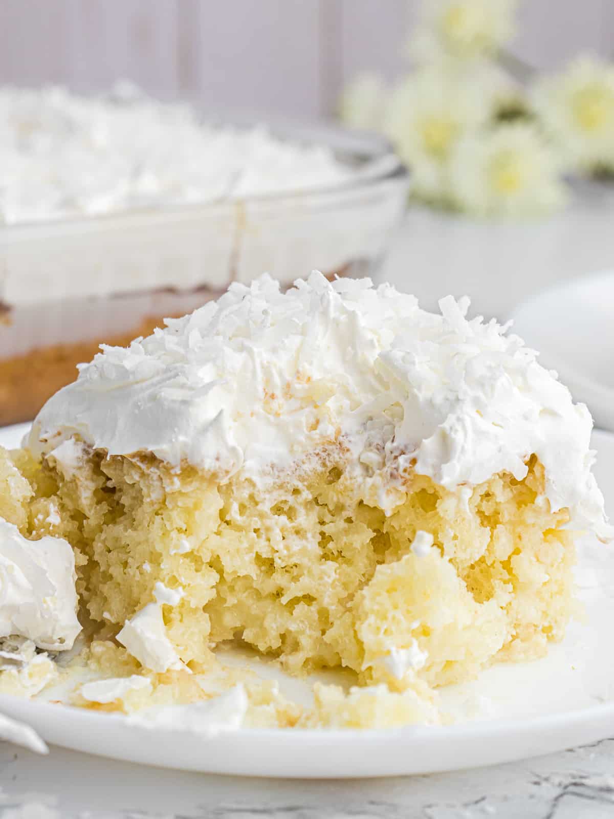 A slice of coconut cream poke cake with a bite missing on a white plate.