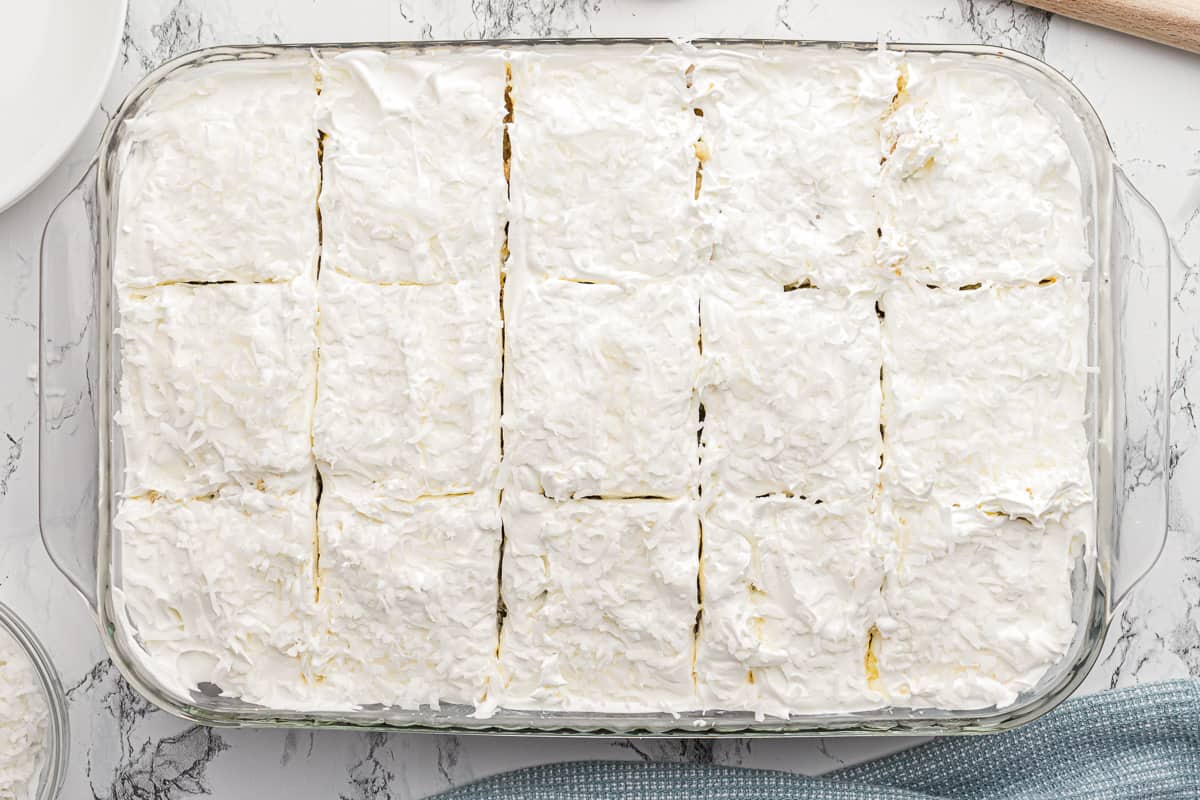 A top down shot of a coconut cake in a 13 by 9 baking dish cut into 15 slices.