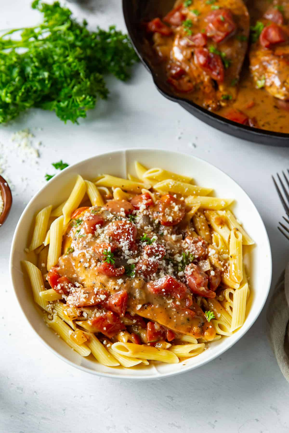Chicken with tomatoes in sauce over cooked pasta in a bowl.