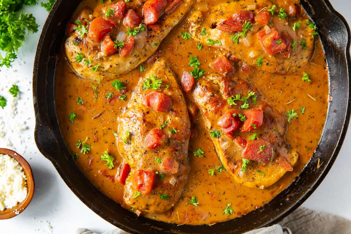 Chicken with tomatoes in sauce in a cast iron skillet.