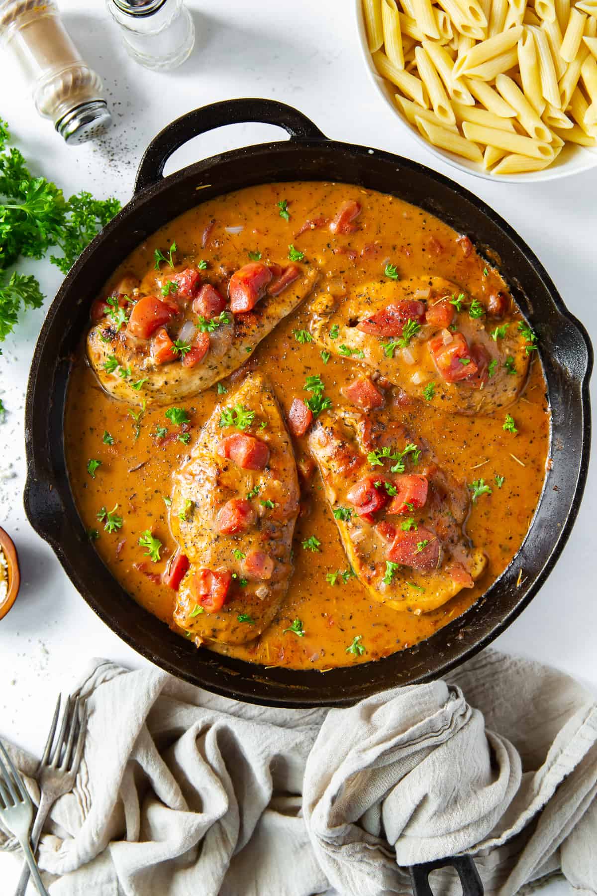 A top down shot of chicken in a tomato cream sauce in a cast iron skillet.