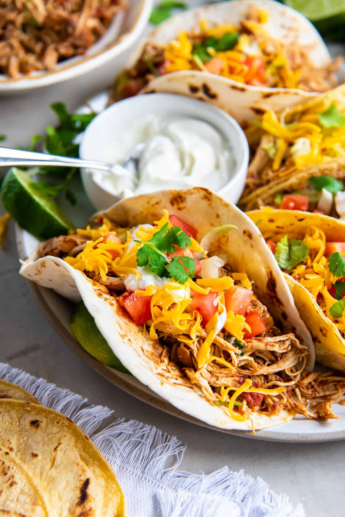 Chicken tacos topped with cilantro and tomato on a platter with a small bowl of sour cream.