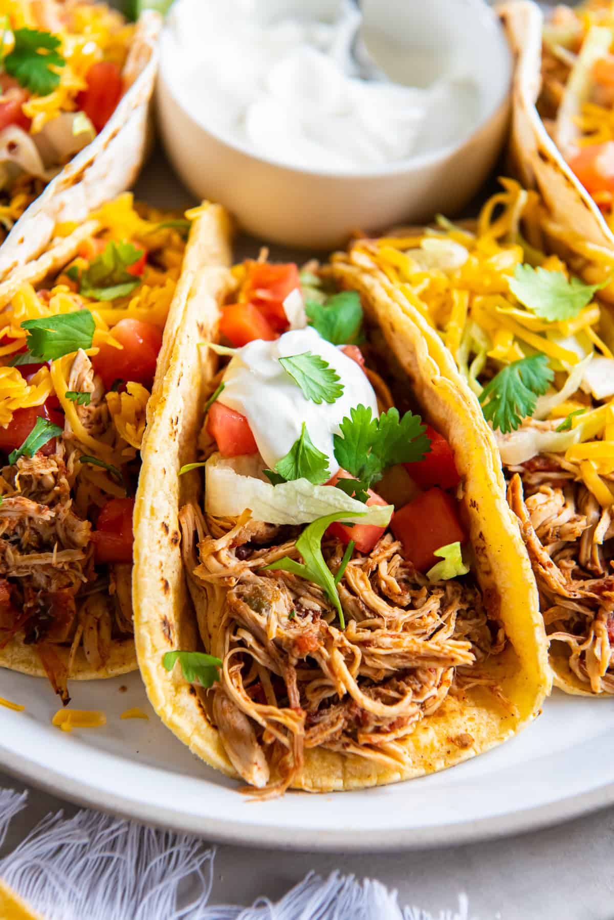 Chicken tacos topped with sour cream, tomato, and cilantro on a platter.