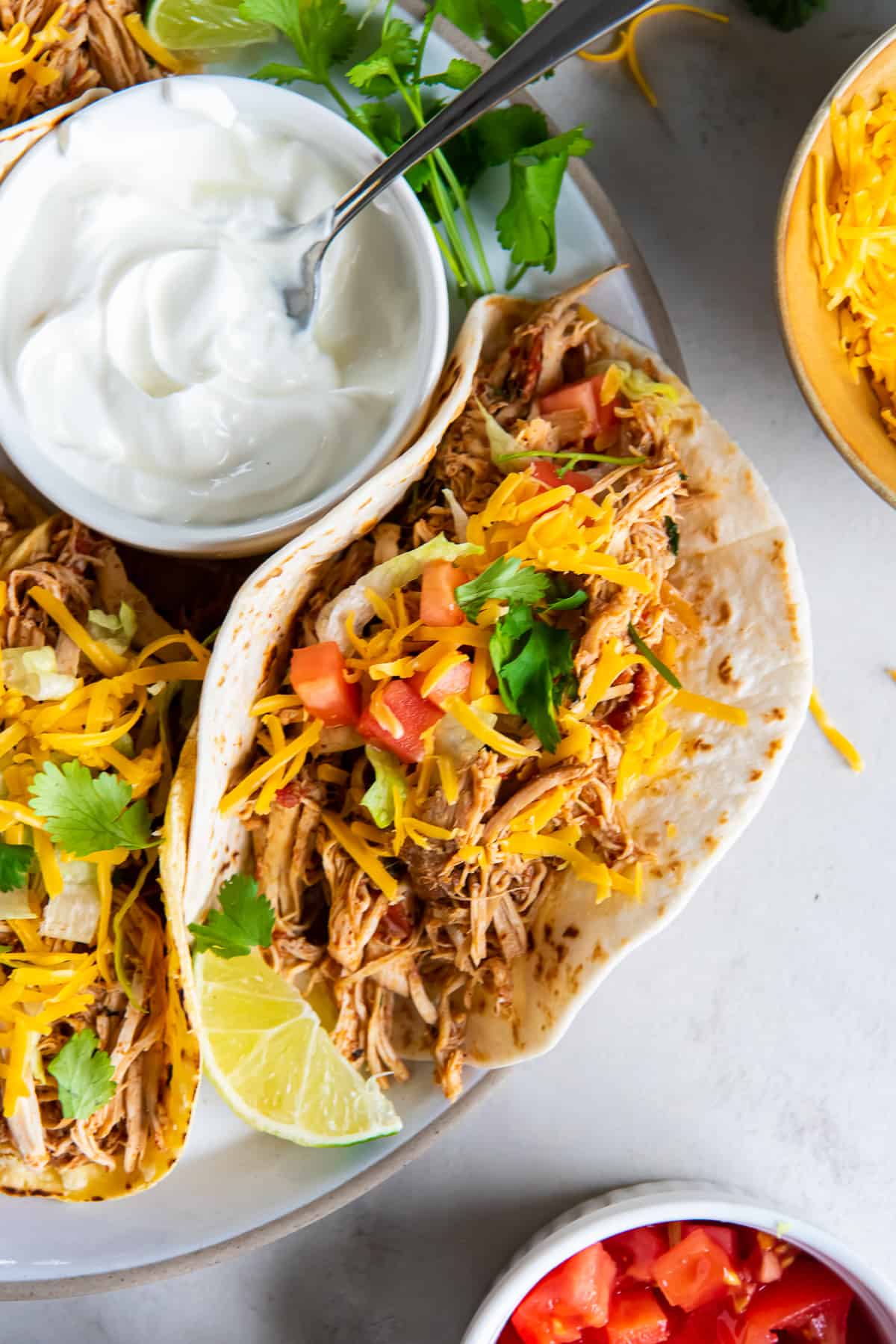 A top down shot of a chicken taco on a platter with a small bowl of sour cream.