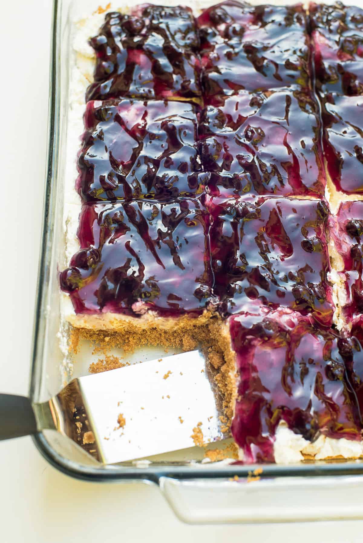 A spatula in a dish of blueberry cheesecake dessert.