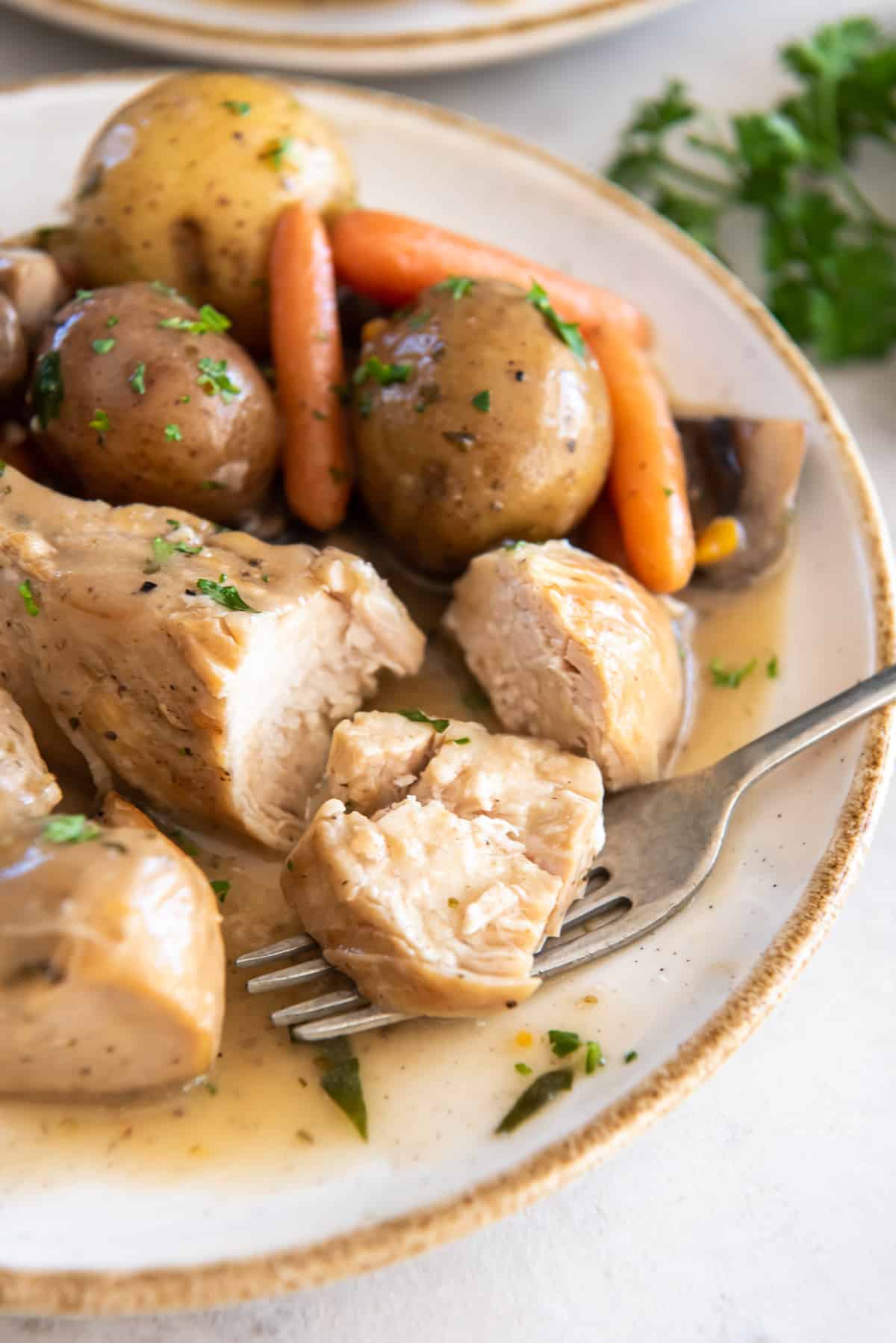 A fork on a plate after breaking into a piece of chicken with gravy.