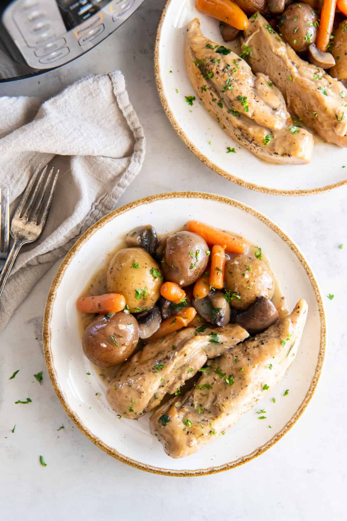 A top down shot of two plates filled with Ranch chicken with potatoes, carrots, and mushrooms next to an Instant Pot.