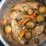 A top down closeup of chicken, potatoes and carrots in a creamy gravy in an Instant Pot.