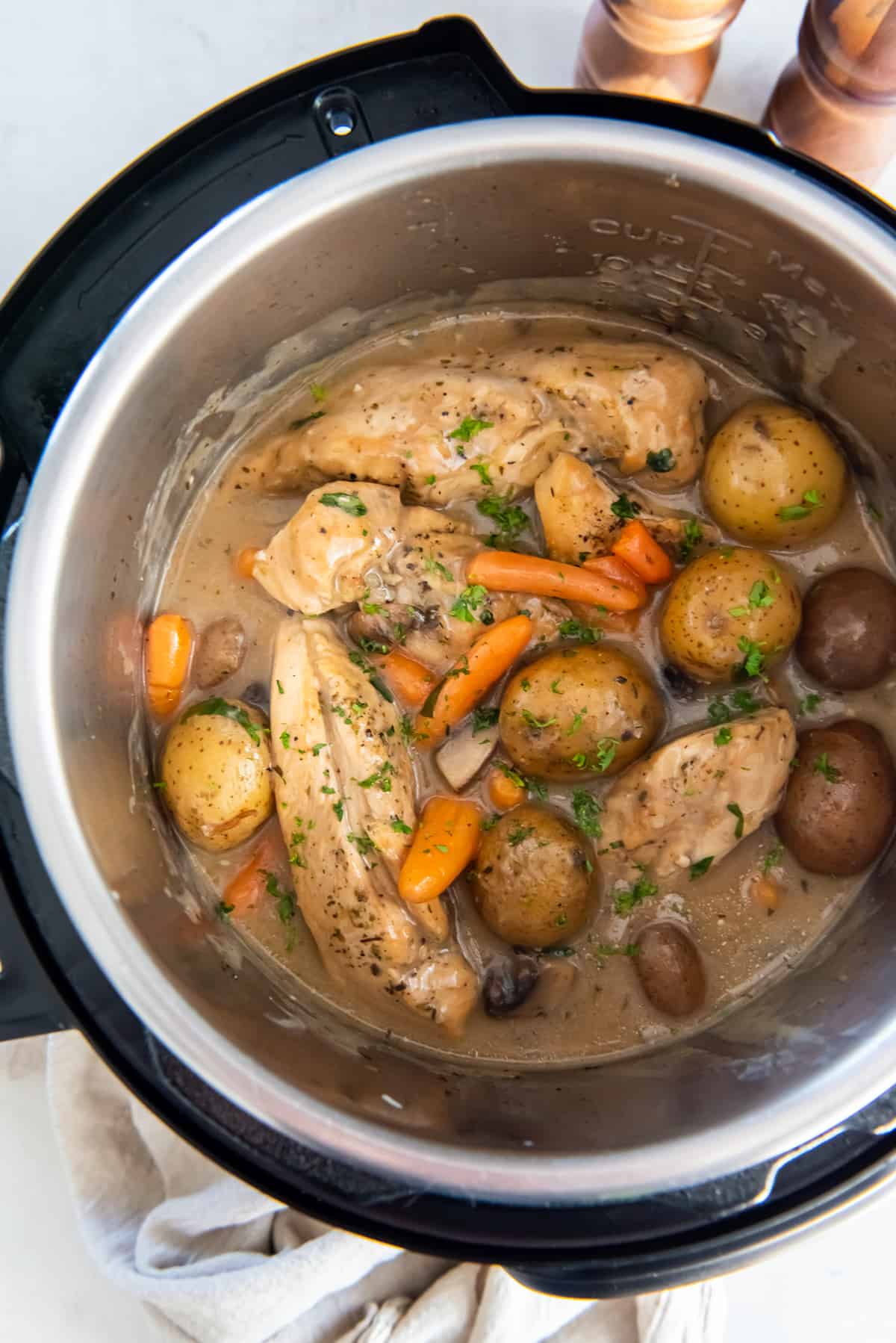 A top down closeup of chicken, potatoes and carrots in a creamy gravy in an Instant Pot.