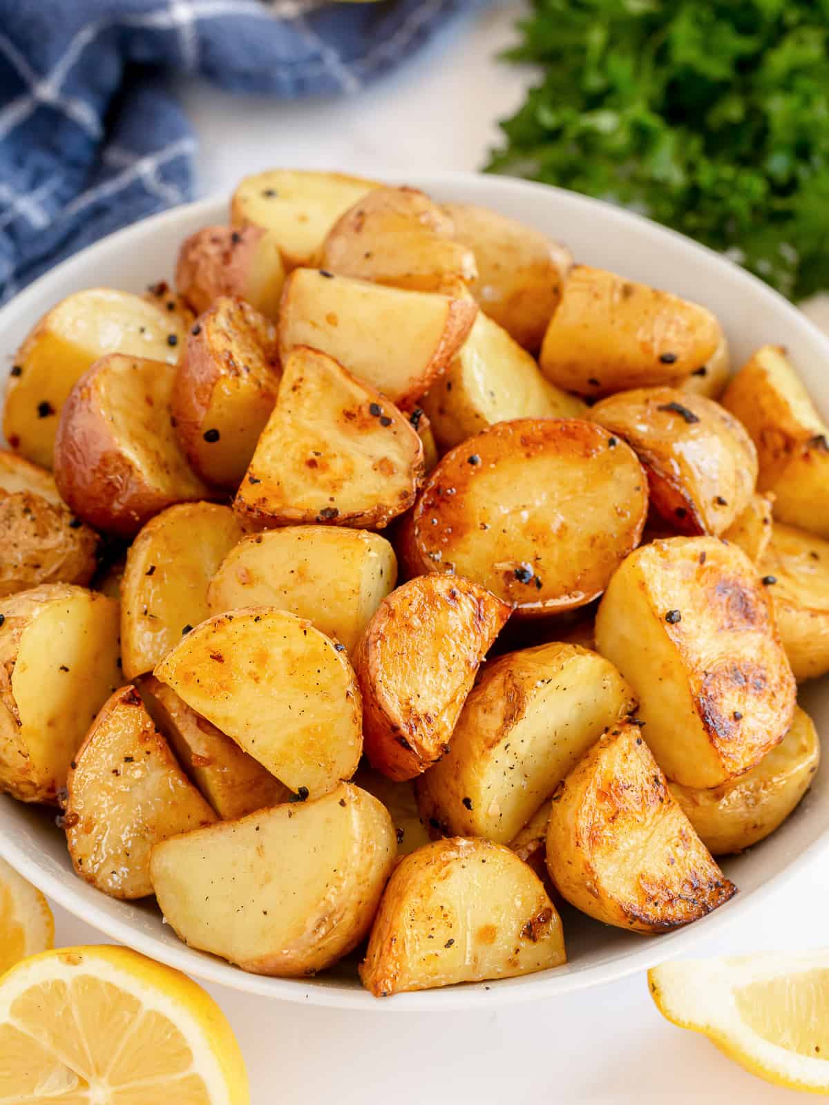 Roasted lemon and garlic potatoes in a white bowl next to lemon wedges and parsley.