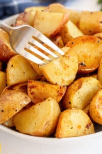 A bowl filled with roasted potatoes with a fork piercing one on top.