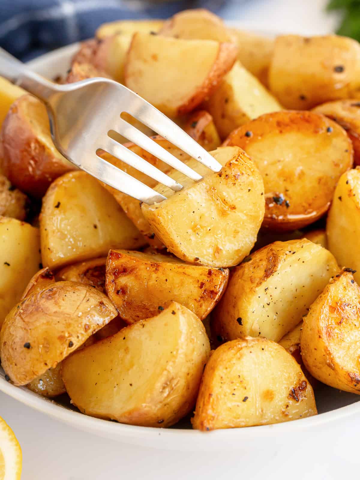 A bowl filled with roasted potatoes with a fork piercing one on top.