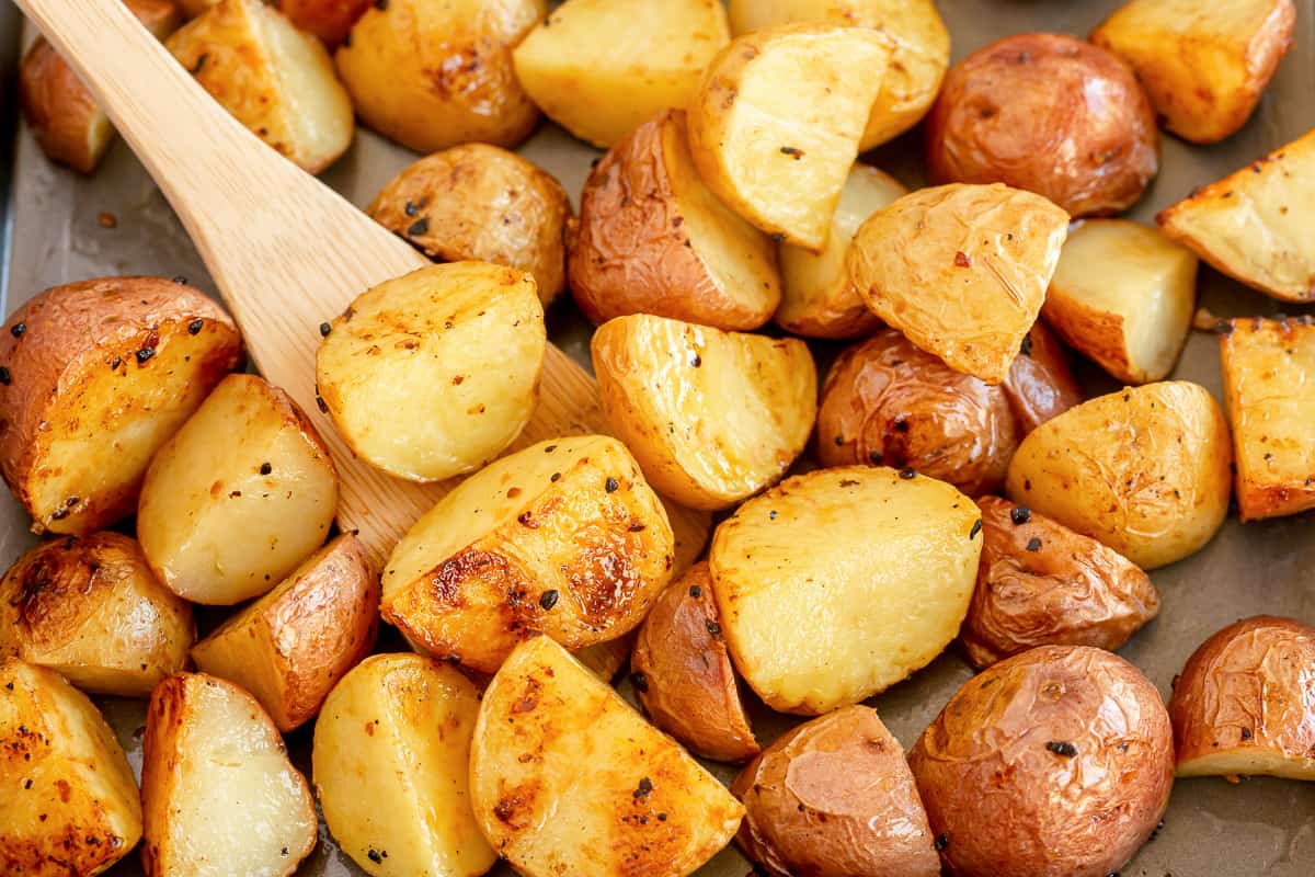 A wooden spoon stirring roasted potatoes on a baking sheet.