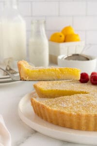 A spatula lifting a slice of lemon tart from a platter.