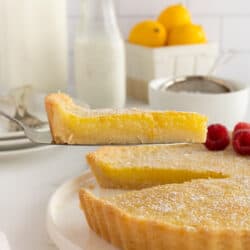 A spatula lifting a slice of lemon tart from a platter.