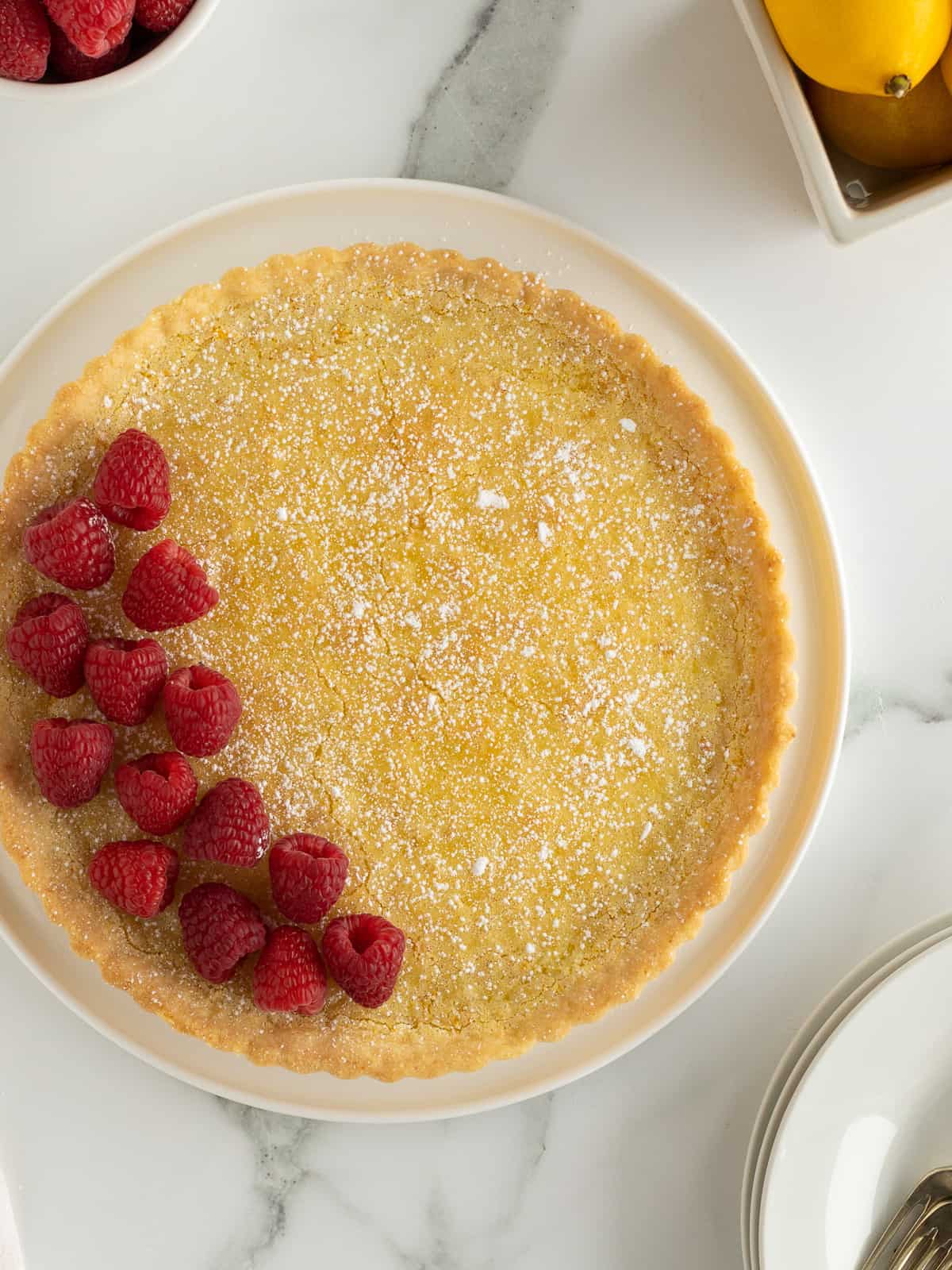 A top down shot of a lemon tart topped with powdered sugar and fresh raspberries.