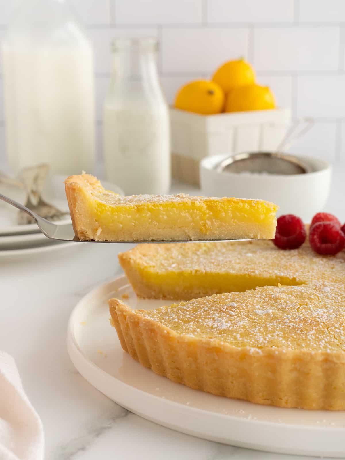 A spatula lifting a slice of lemon tart from a platter.