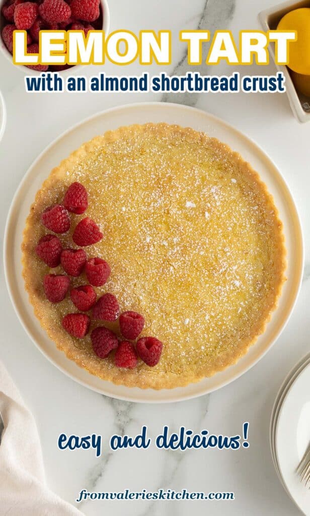 A top down shot of a lemon tart topped with powdered sugar and fresh raspberries with text.