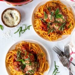 A top down shot of a pot of meatballs and sauce next to two plates of spaghetti.