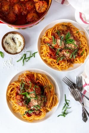 A top down shot of a pot of meatballs and sauce next to two plates of spaghetti.