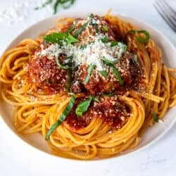 A dinner plate filled with homemade spaghetti and meatballs topped with basil and Parmesan.